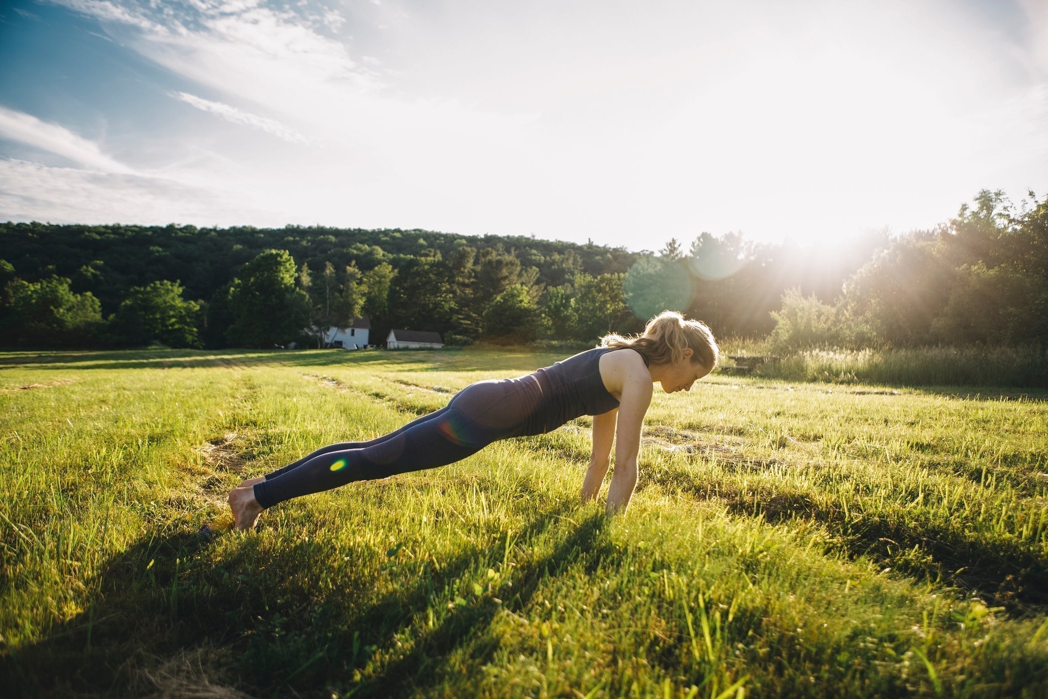 Junge Frau macht Liegestütze in einem Feld bei Sonnenschein