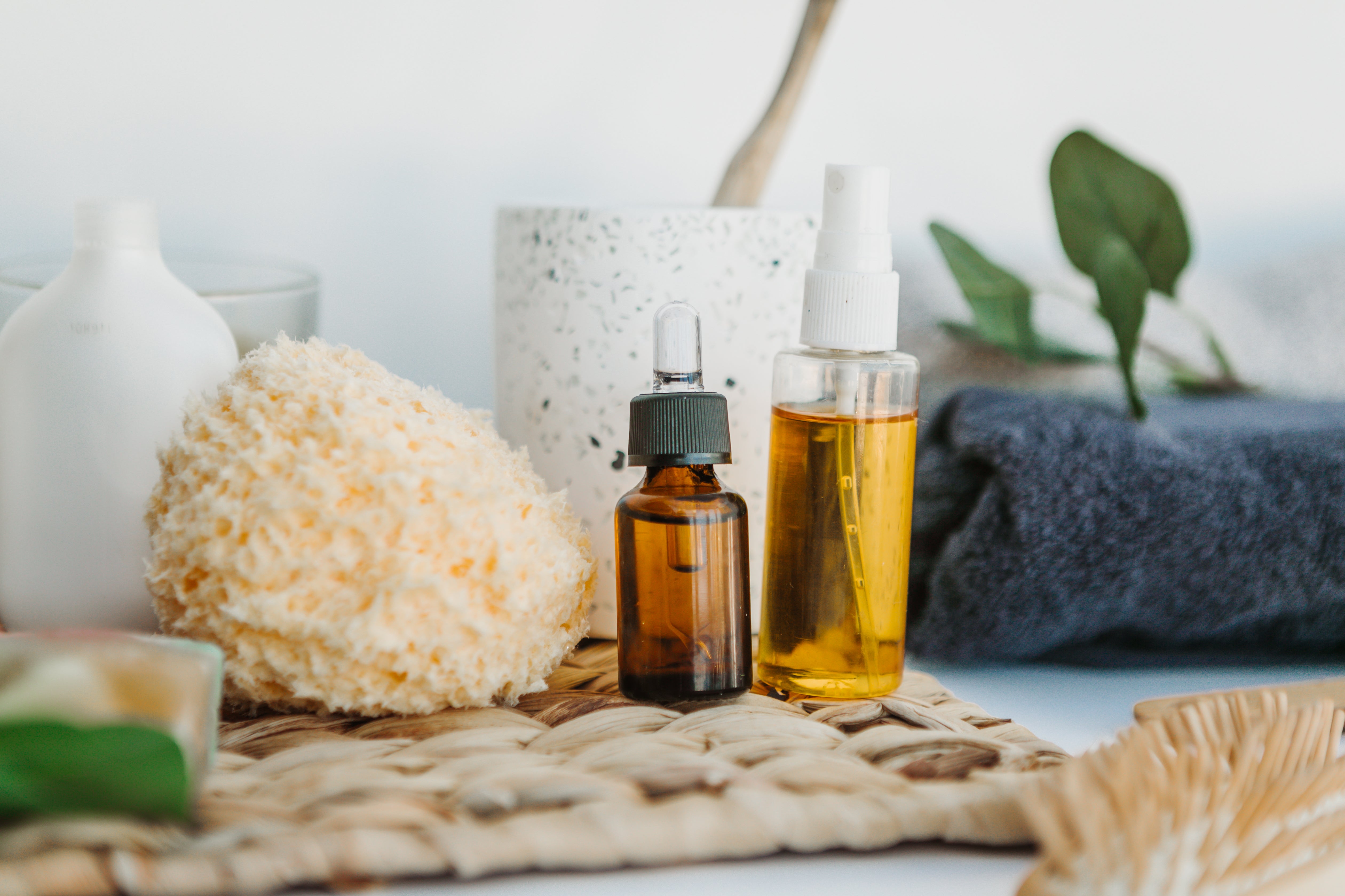 Beauty-Utensilien wie Serum, Schwamm und Bürste stehen nebeneinander auf einer braunen Unterlage vor weißem Hintergrund