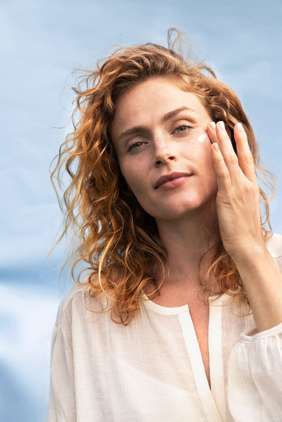 Frau mit lockigem Haar steht im Freien und cremt ihr Gesicht ein