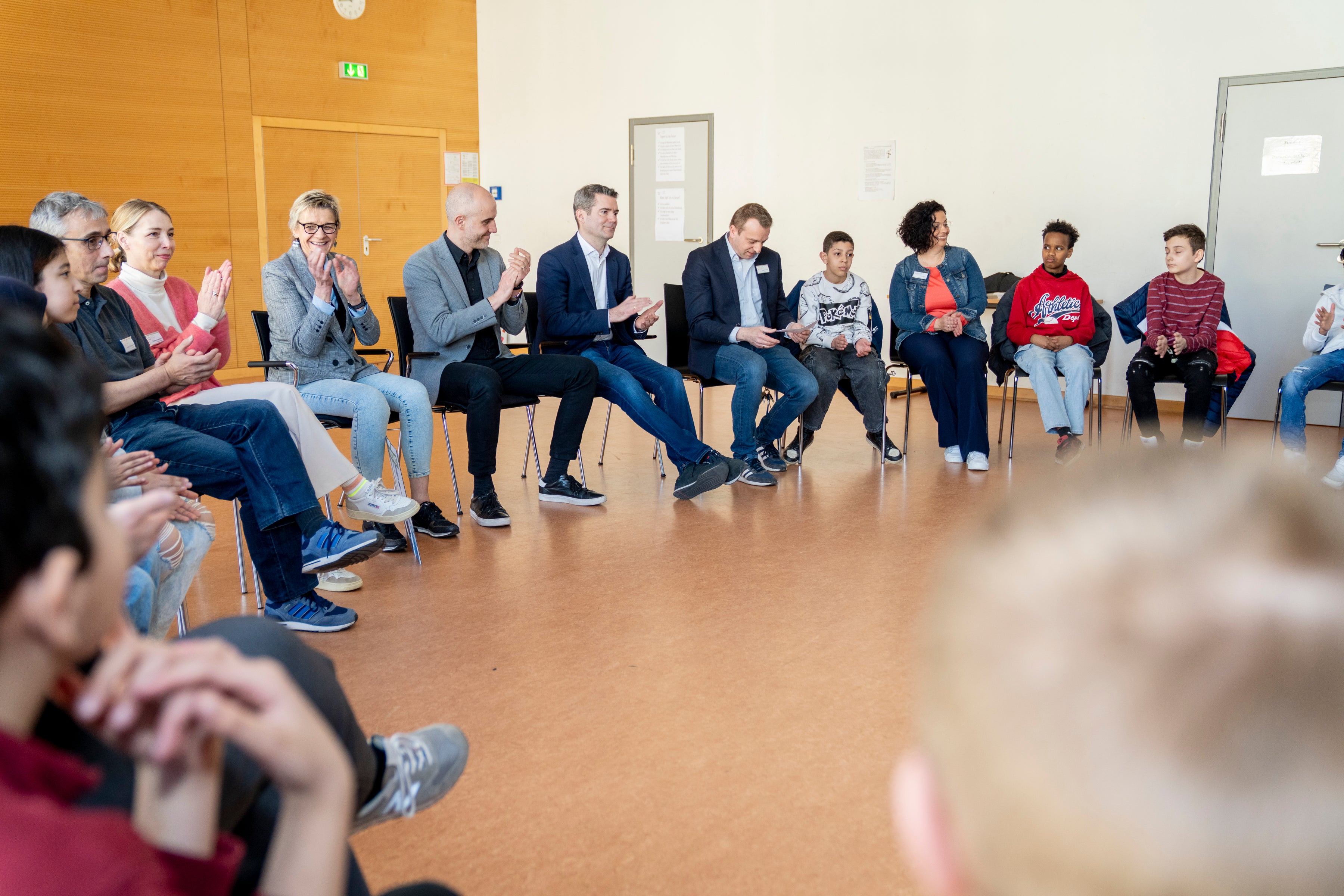 Kinder und Erwachsene sitzen in einem Stuhlkreis und klatschen