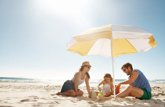 Familie mit Kind unter Sonnenschirm am Strand beim Spielen im Sand