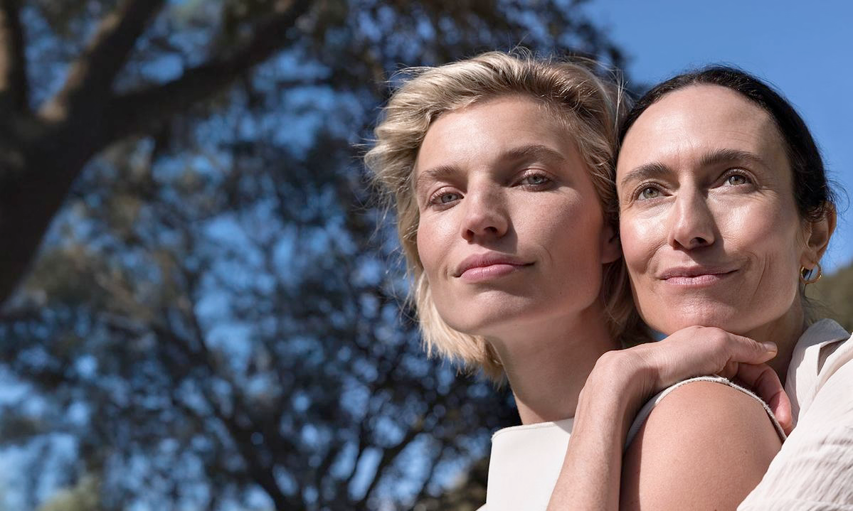 Zwei Frauen in der Sonne, eine umarmt die andere, natürlicher Look im Freien