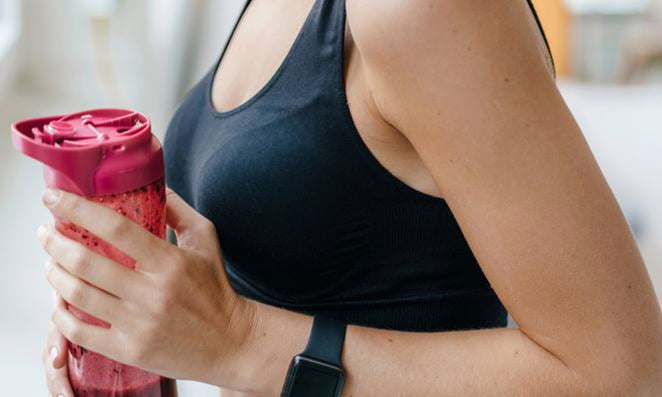 Aufnahme eines weiblichen Oberkörpers in einem Sport-Top die eine Trinkflasche trägt