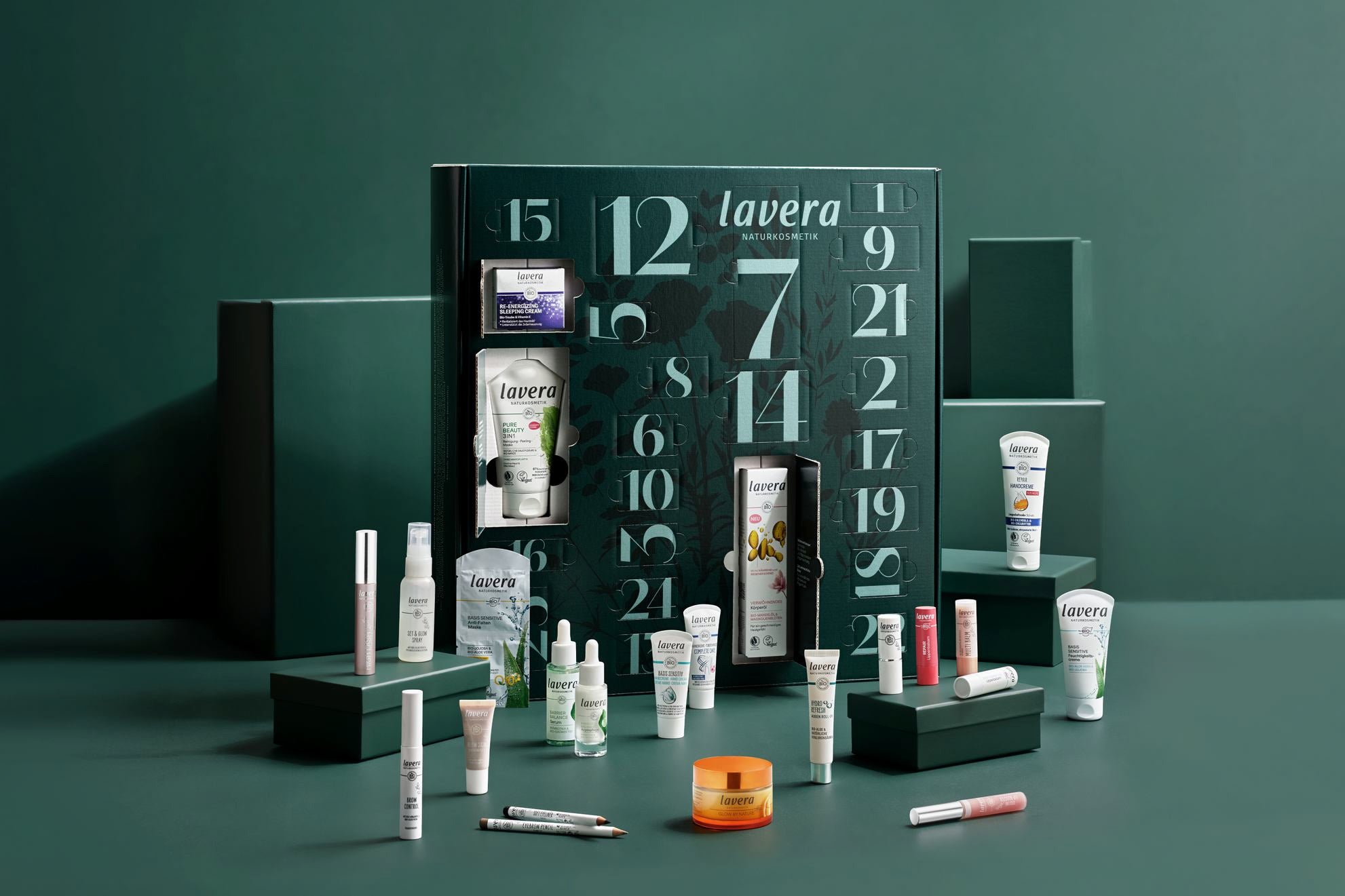 Geöffneter lavera Adventskalender mit Mini-Pflegeprodukten und Make-up auf grünem Set