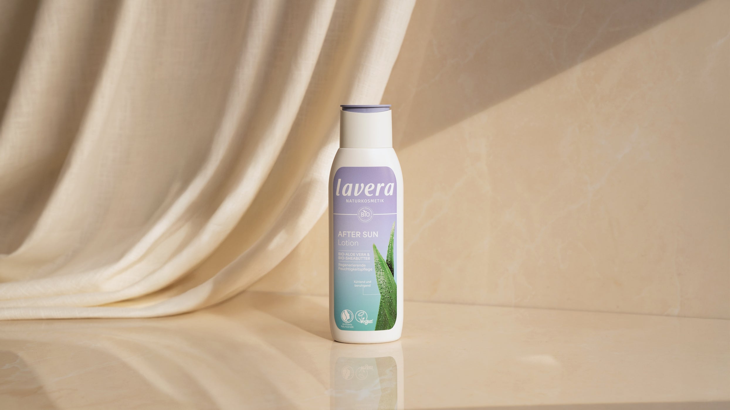 lavera After Sun Lotion Flasche vor beigem Hintergrund mit Stoff, Produktfoto