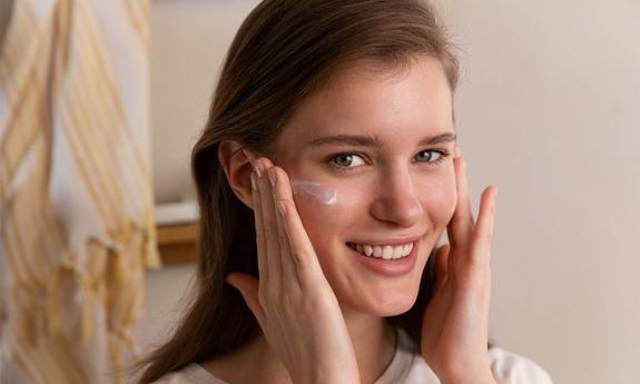 Frau trägt Anti-UV-Fluid lächelnd auf die Wange auf