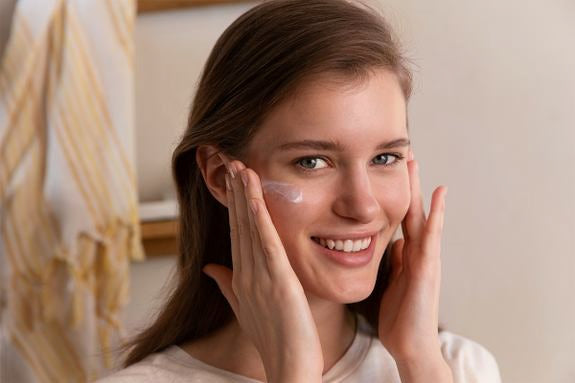 Frau trägt Anti-UV-Fluid lächelnd auf die Wange auf