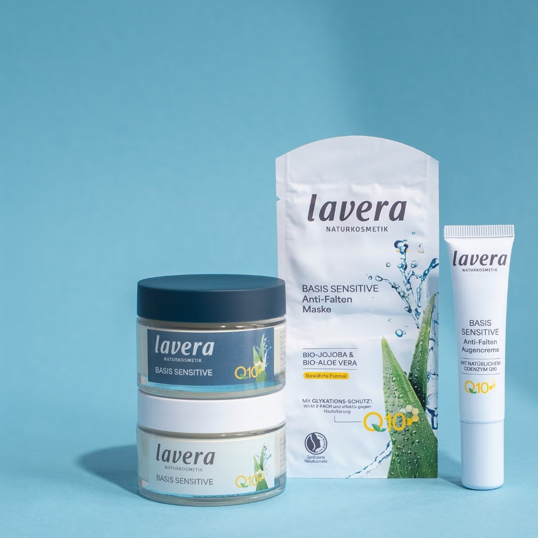 Vier lavera Basis Sensitive Anti-Falten-Produkte mit Q10 stehen vor hellblauem Hintergrund: zwei Cremetiegel, eine Tuchmaske und eine Augencreme.