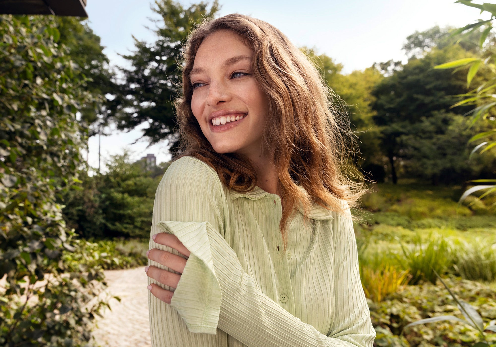 Frau lächelt links an der Kamera vorbei und steht im Park