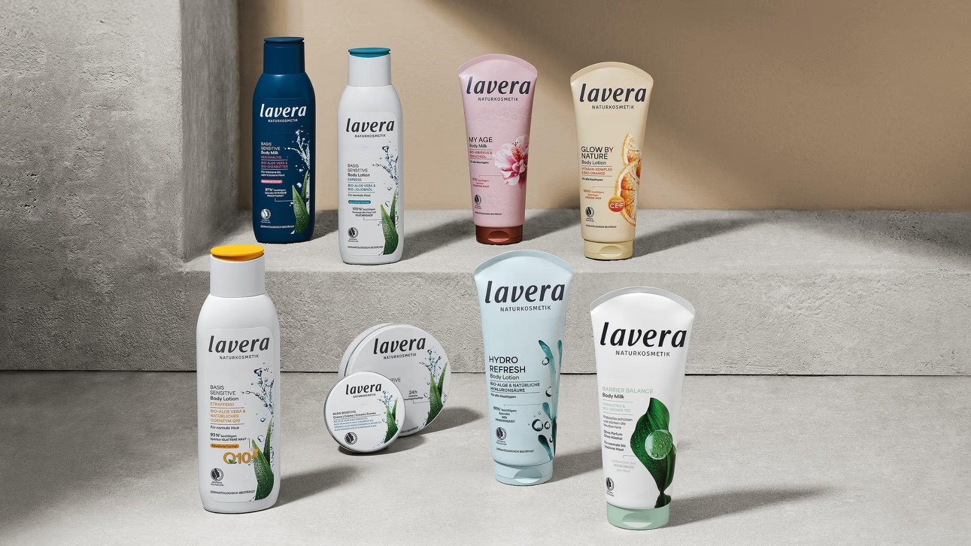 Neun lavera Körperpflegeprodukte, darunter Lotionen, Körpermilch und Cremes auf gestuften Betonsockeln in einem modern beleuchteten Raum stehend.