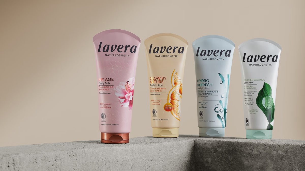Vier lavera Körperlotionen der Linien My Age, Glow by Nature, Hydro Refresh und Barrier Balance stehen auf grauen Betonsockeln vor neutralem Hintergrund.