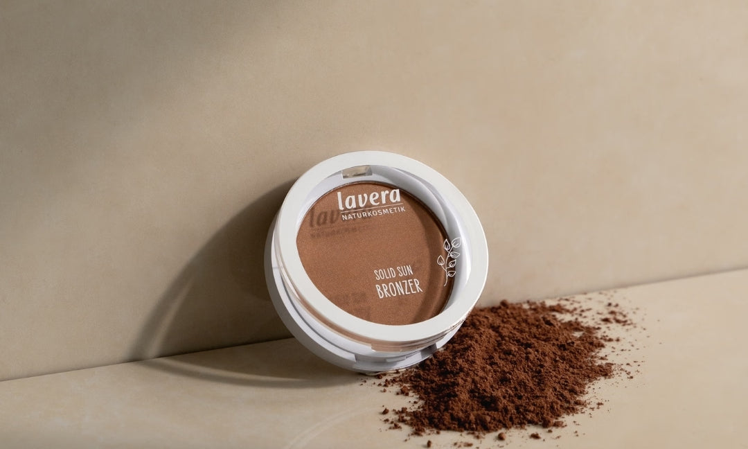 lavera Solid Sun Bronzer liegt auf einer beigefarbenen Oberfläche neben verstreutem Bronzerpuder.