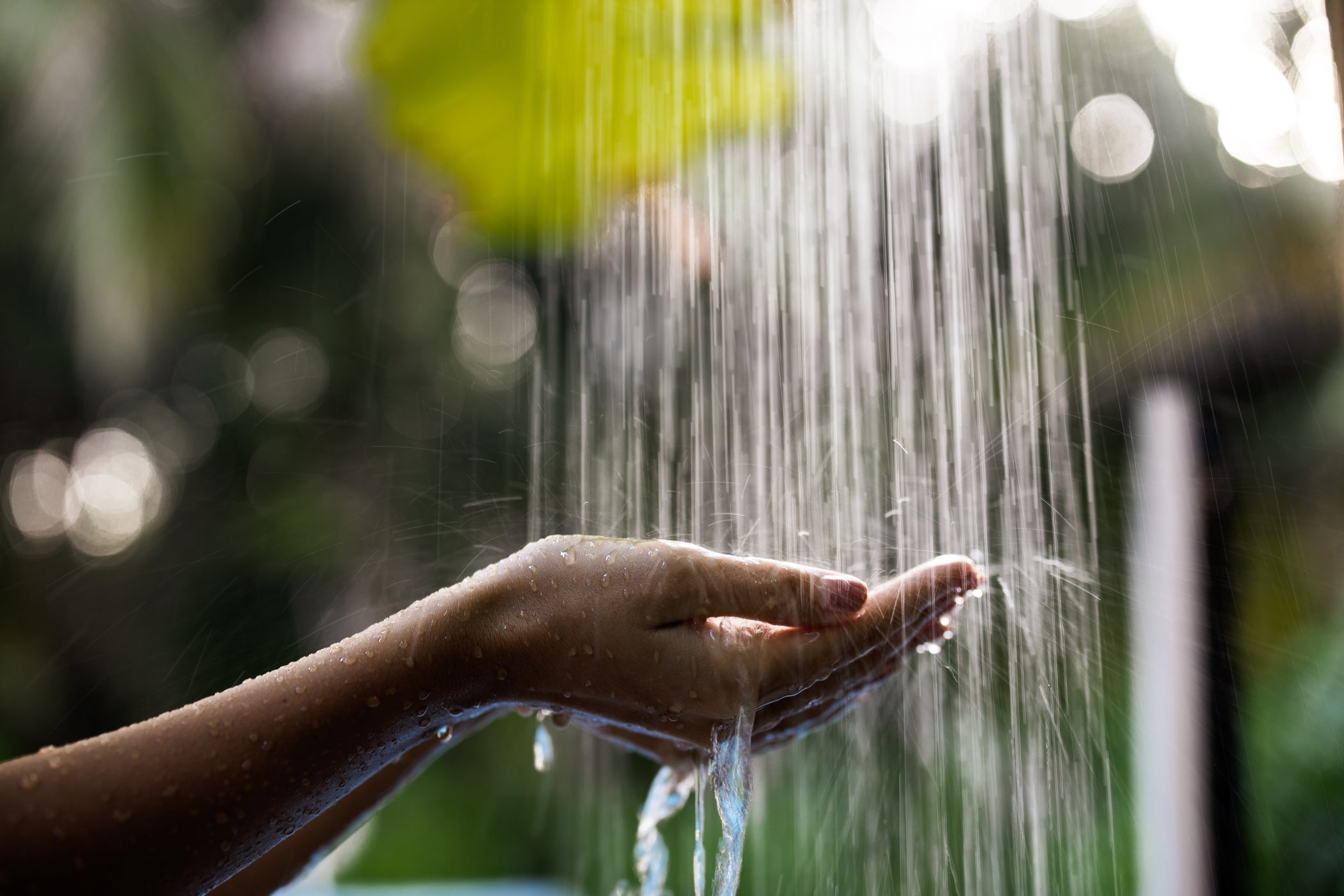 Zwei Hände werden unter das fließende Wasser einer Dusche gehalten – mit blurry Hintergrund