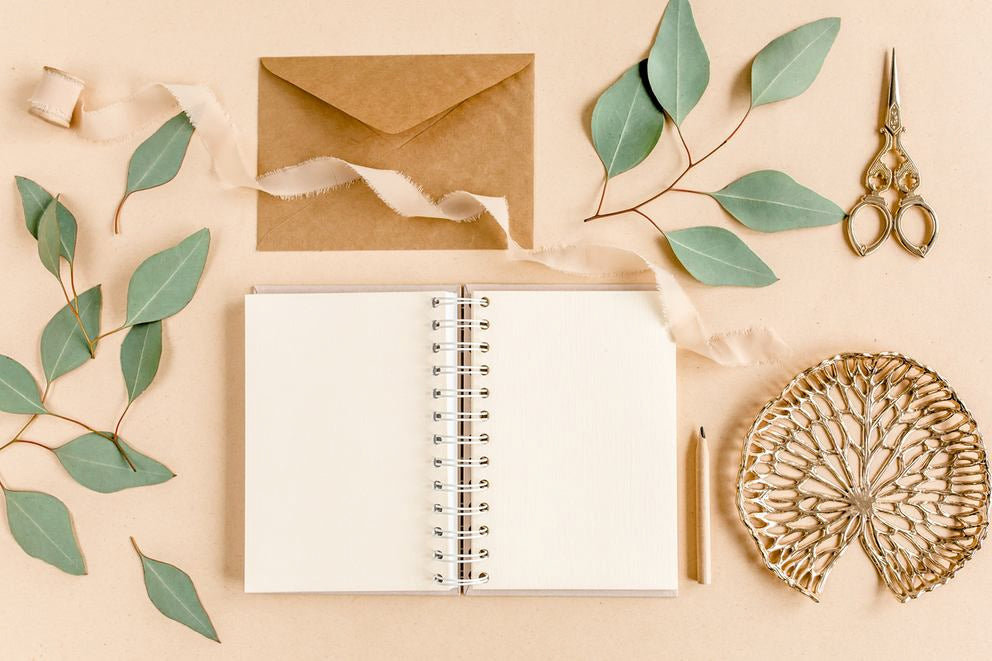 Blanko-Notizbuch mit Umschlag, Eukalyptusblättern, Schere und Deko im Flatlay