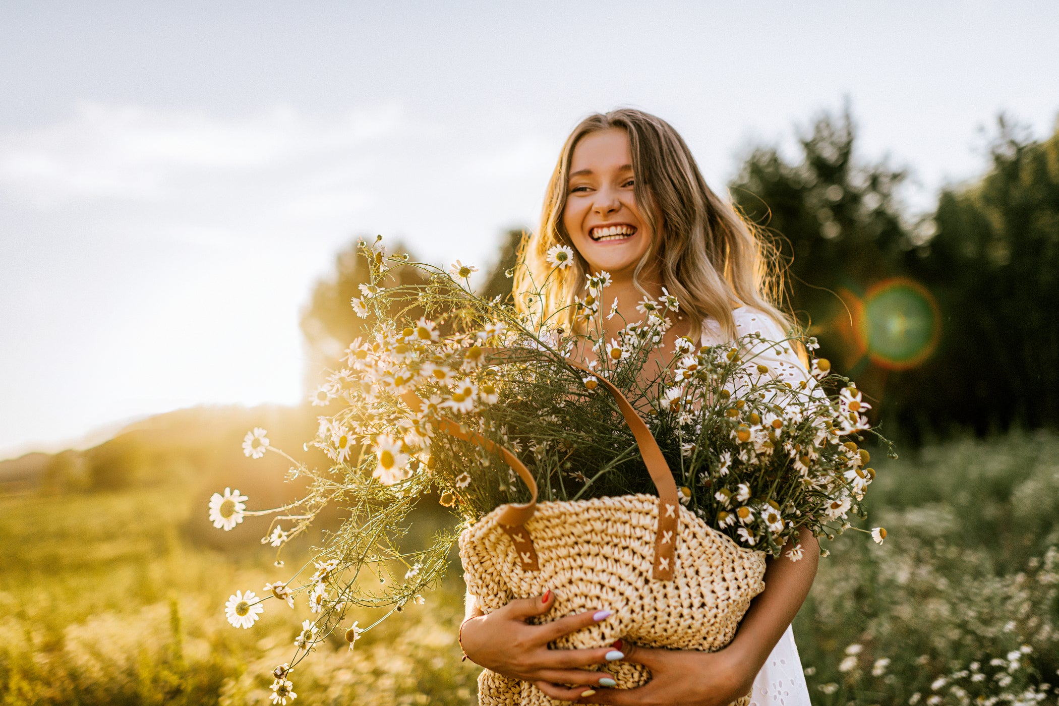 Junge Frau mit Sommerkleid geht mit einem Beutel voller Blumen durch ein Feld