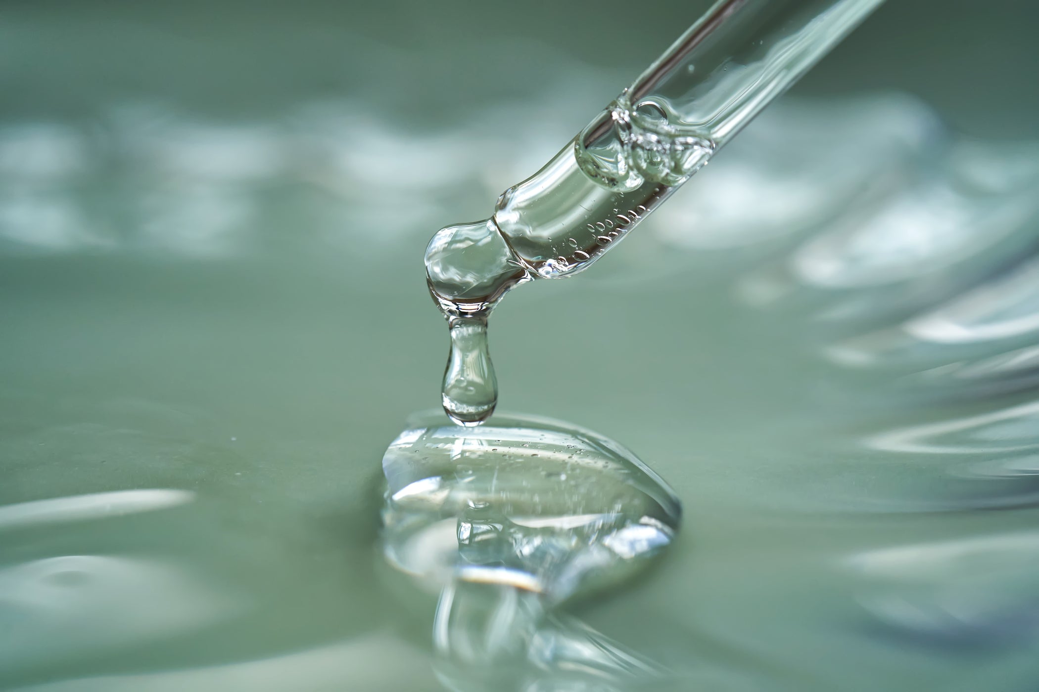 Pipette tropft klares Serum auf glänzende Geloberfläche, Makroaufnahme