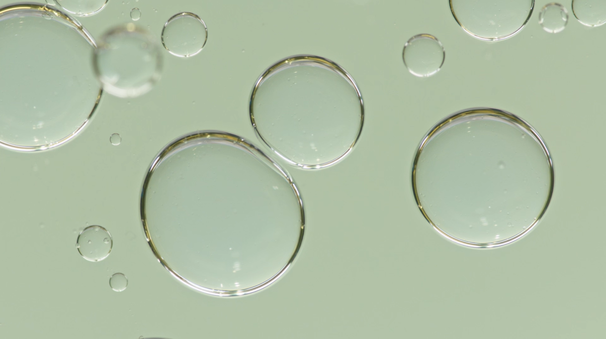 Große und kleine Tropfen einer Flüssigkeit in Nahaufnahme auf grünem Hintergrund.