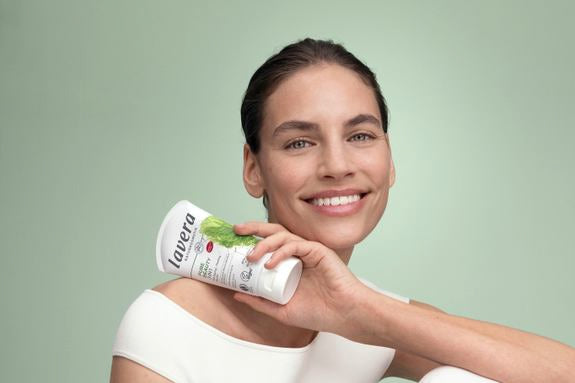 Lächelnde Frau hält ein lavera Pure Beauty Produkt vor grünem Hintergrund