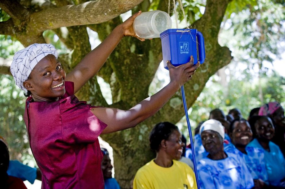 Dunkelhäutige Frau mit Turban gießt Wasser in einen selbstgebauten Trichter