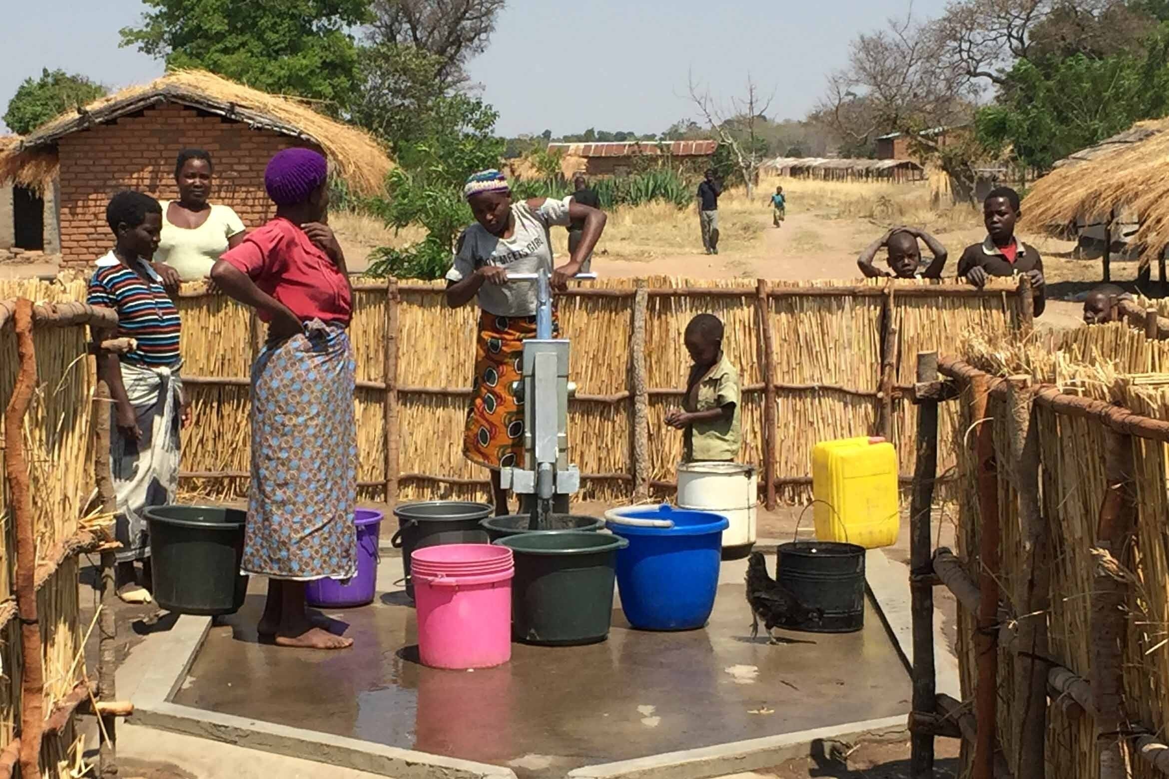 Gruppe afrikanischer Frauen und Kinder, die Wasser aus einem Brunnen pumpen