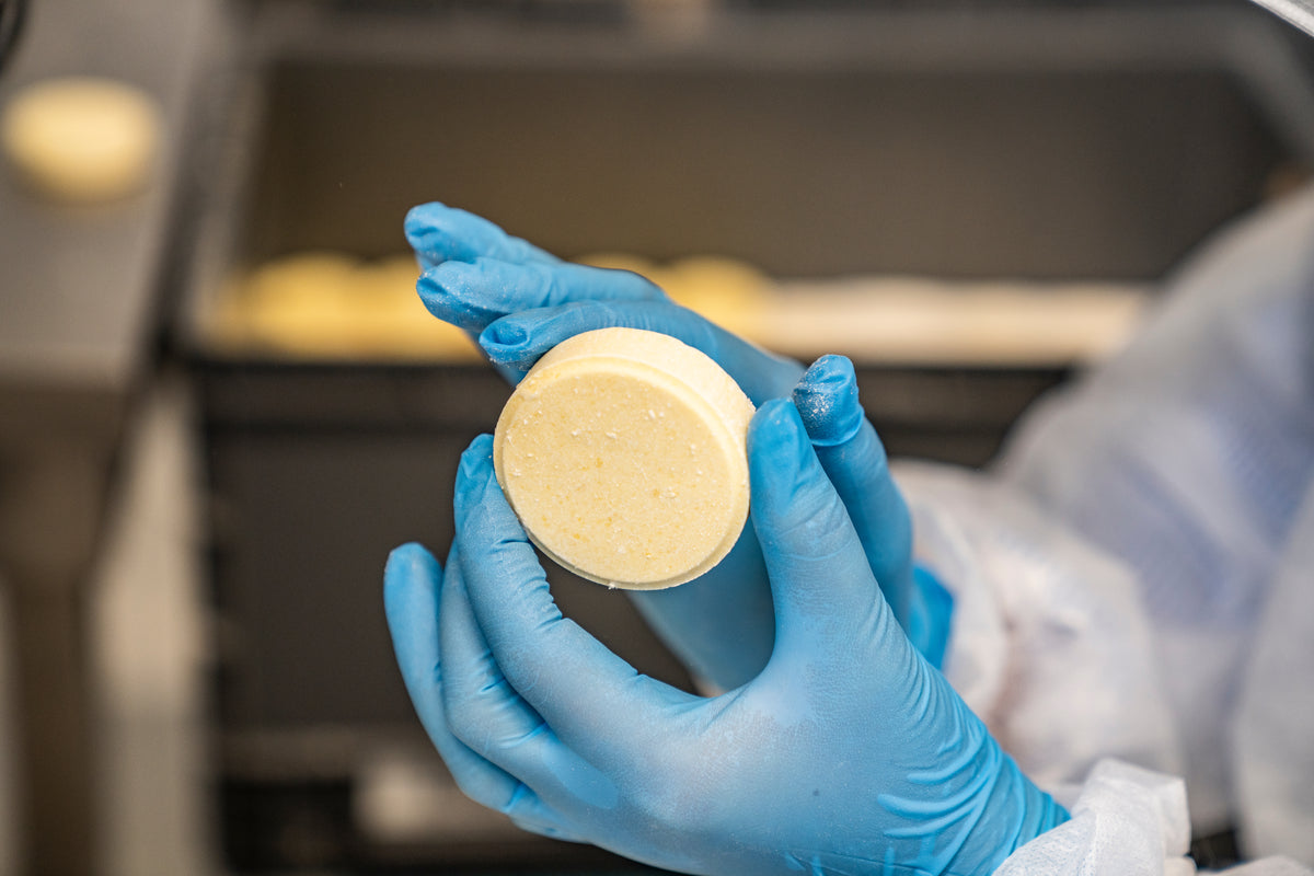 Zwei Hände in blauen Handschuhen halten ein festes Shampoo