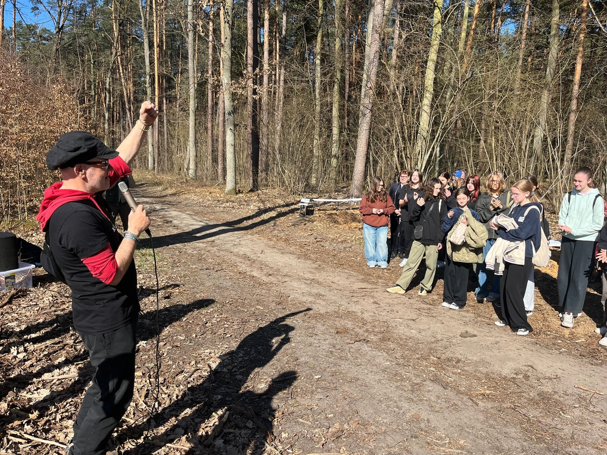 Mann mit Mikrofon steht vor einer Gruppe von Kindern und Jugendlichen und streckt eine Faust in die Höhe