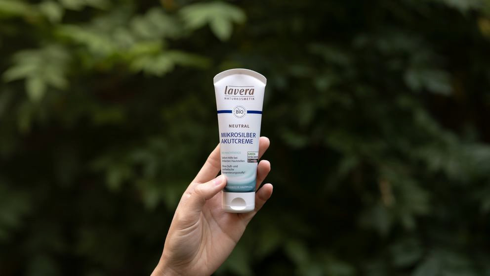 Hand hält lavera Neutral Akutcreme vor Blätterhintergrund