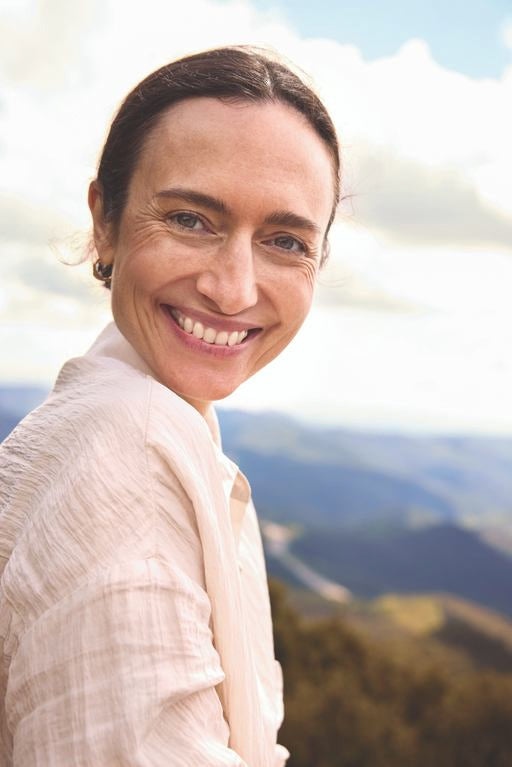 Junge Frau mit braunen Haaren, die in der Natur ist und in die Kamera lächelt