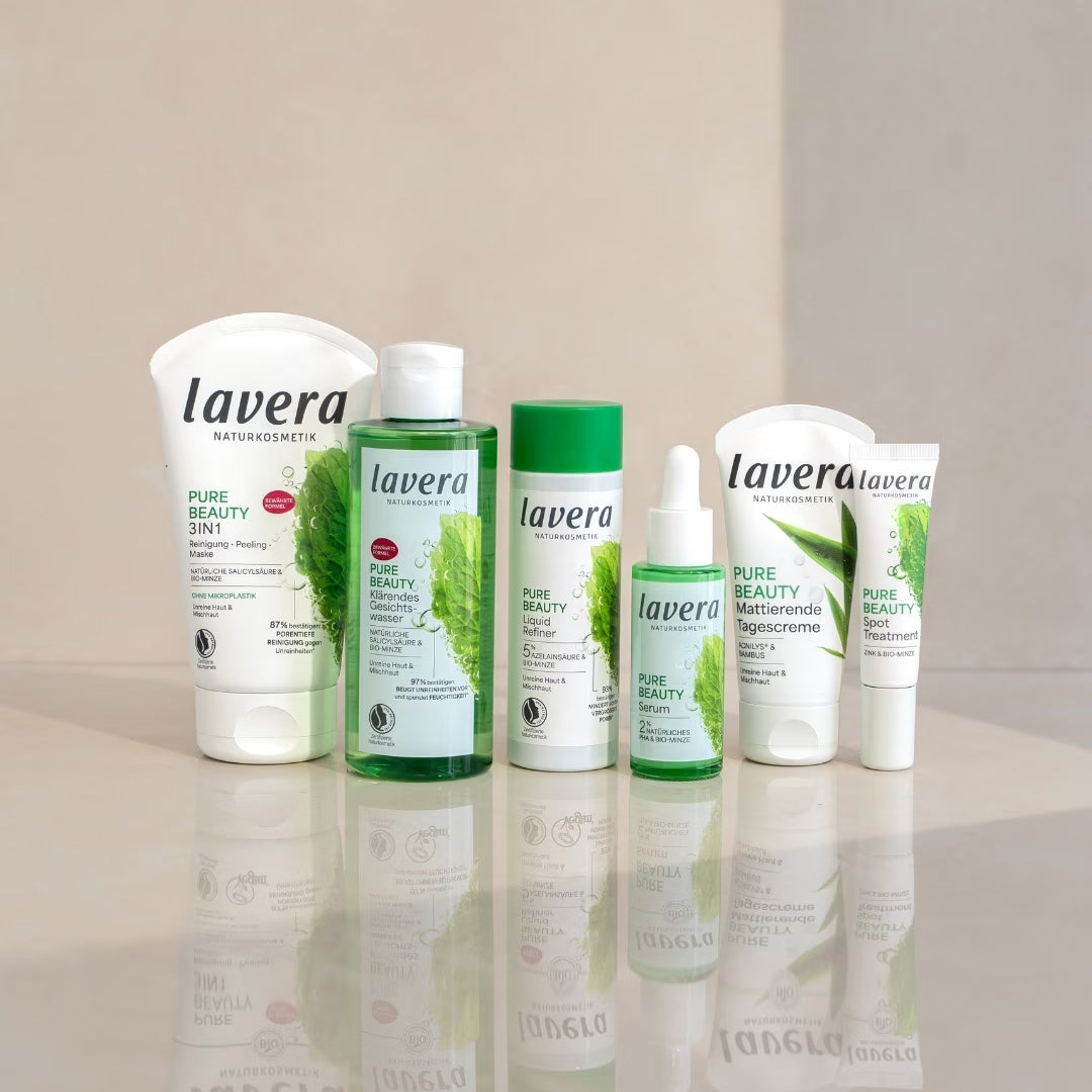 lavera Pure Beauty Gesichtspflegeprodukte stehen auf einer spiegelnden Oberfläche vor einem hellen, zweigeteilten Hintergrund.