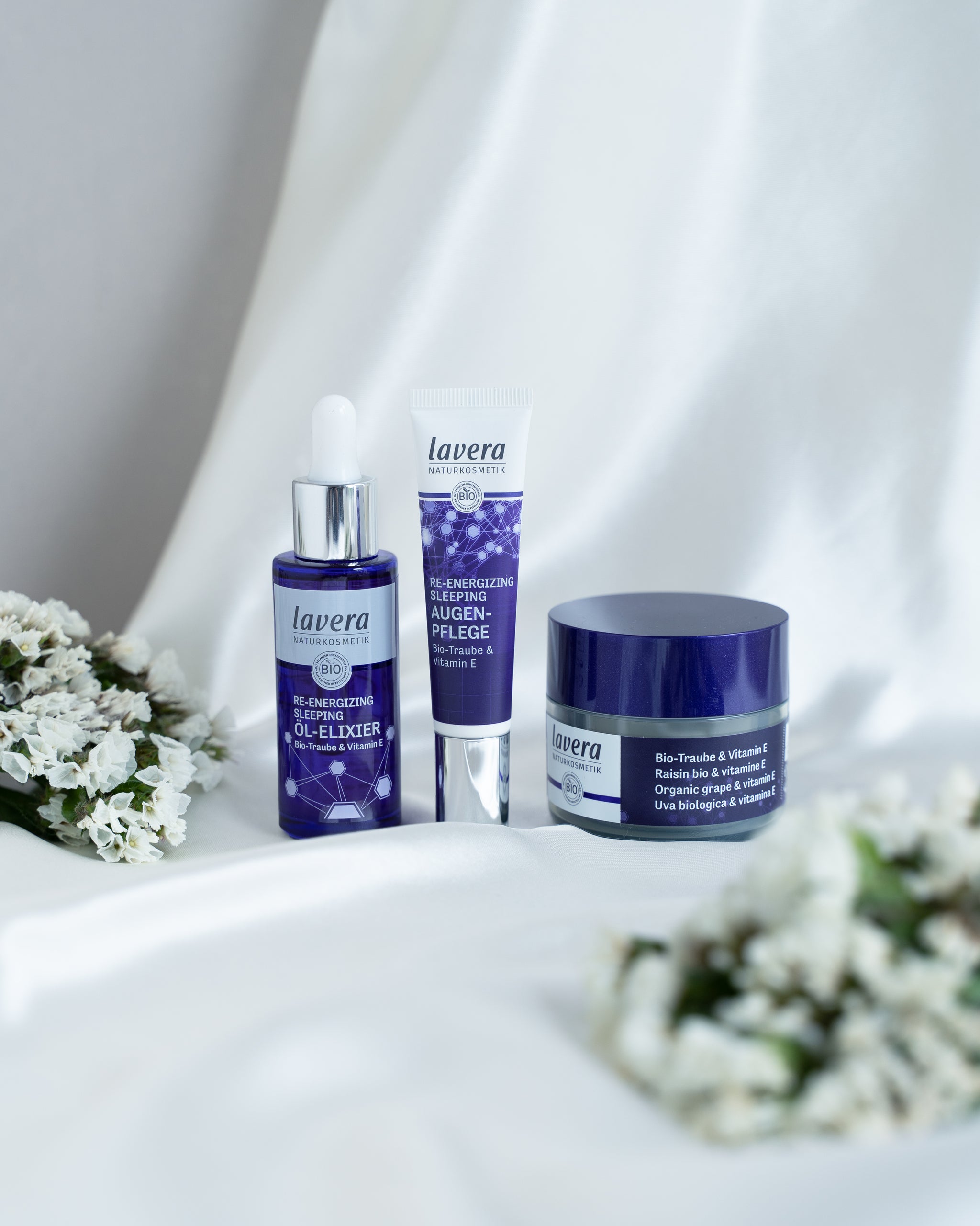 Lavera Re-Energizing Sleeping Pflegeprodukte mit Bio-Traube und Vitamin E, dekorativ mit weißen Blüten arrangiert
