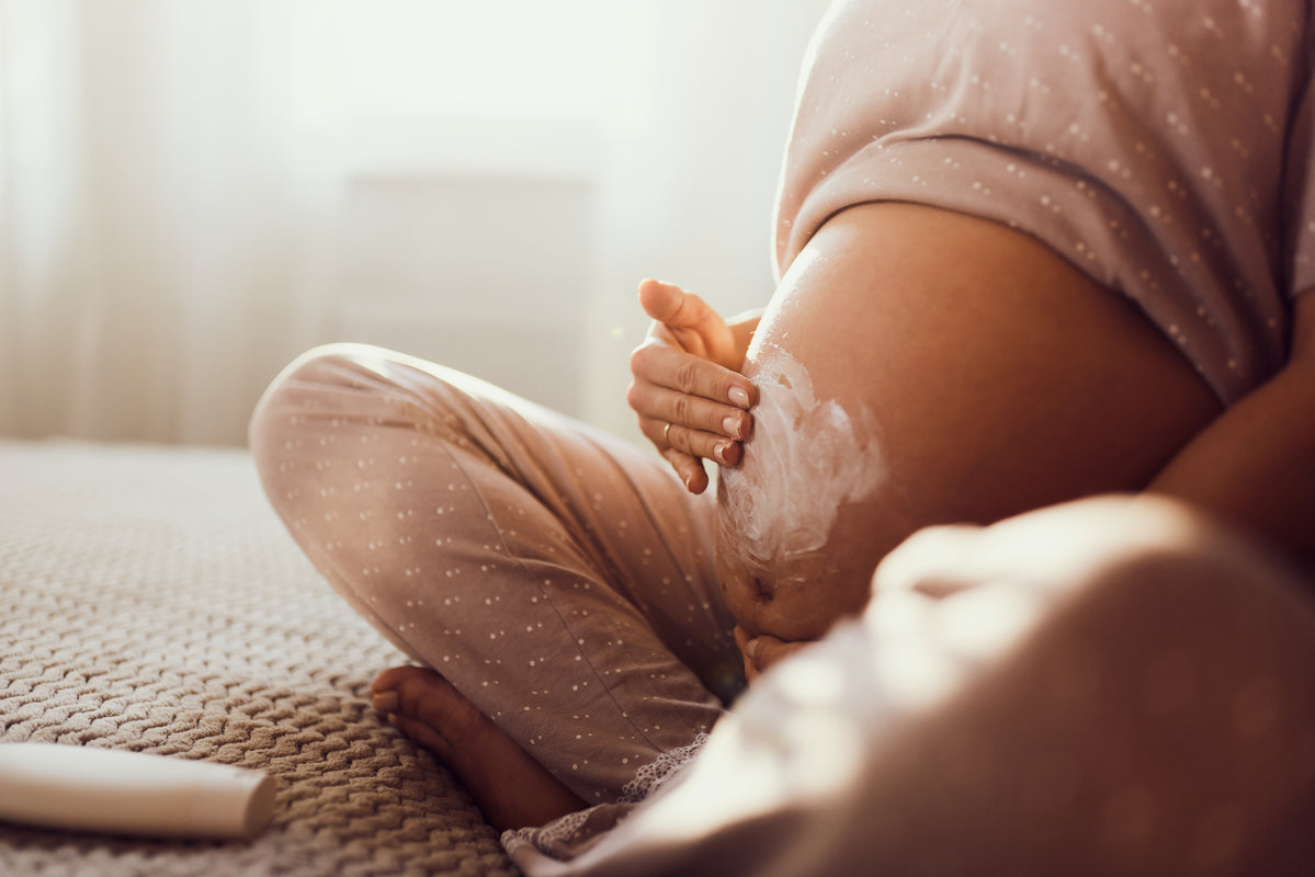 Schwangere Frau in gepunktetem Pyjama cremt ihren Bauch ein 