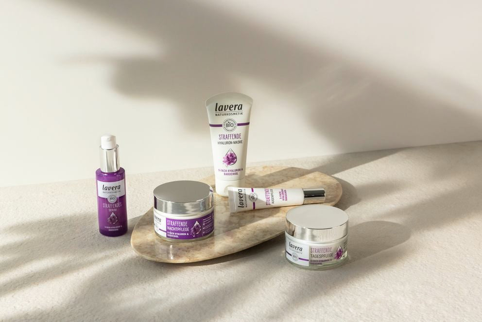 Lavera Straffende Pflegeserie mit fünf lila Produkten auf Stein