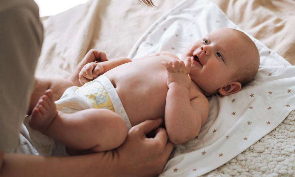 Baby liegt auf Decke, Hände massieren Bauch und Beine, Babypflege