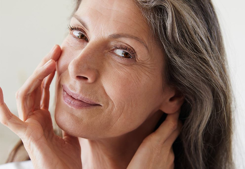 Porträt: Frau mit grauen Haaren berührt Wange und Hals, lächelt