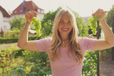 Frau lächelt und hält grüne Weintrauben in die Höhe