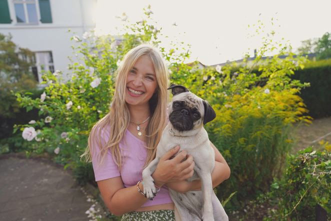 Frau hält einen Mops im Arm und lächelt im Garten