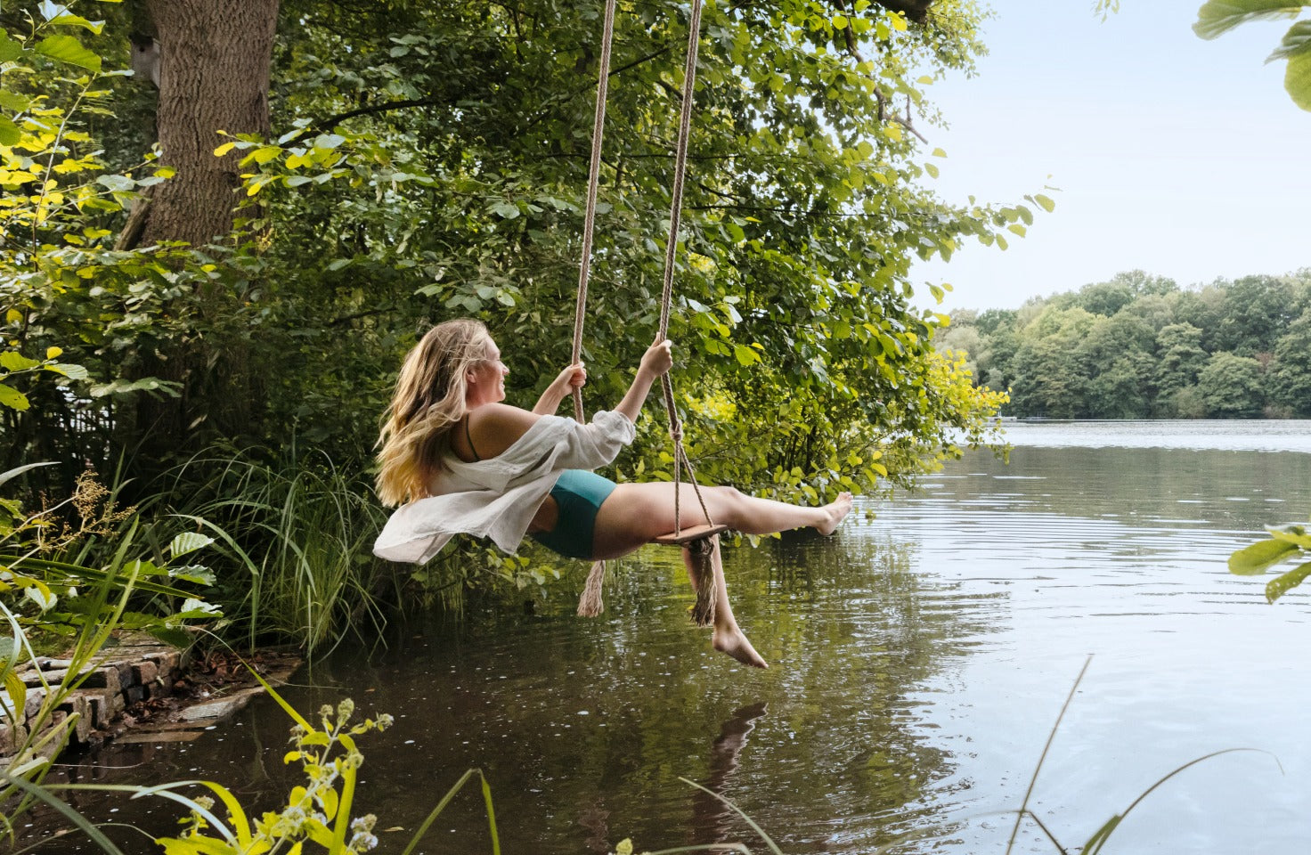 Frau auf einer Seilschaukel über einem See im Wald.