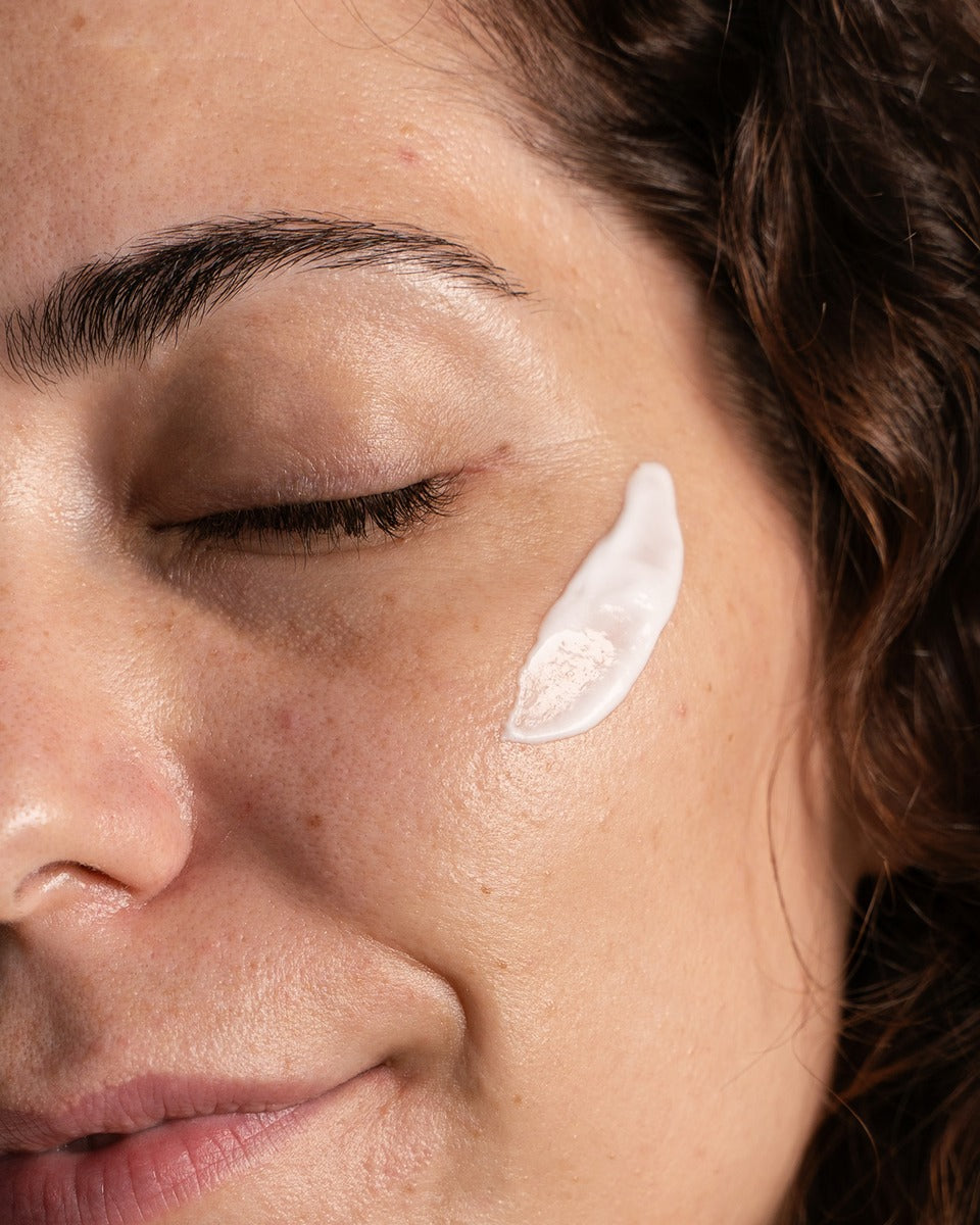 Frau mit geschlossenen Augen, Creme auf der Wange (Nahaufnahme).