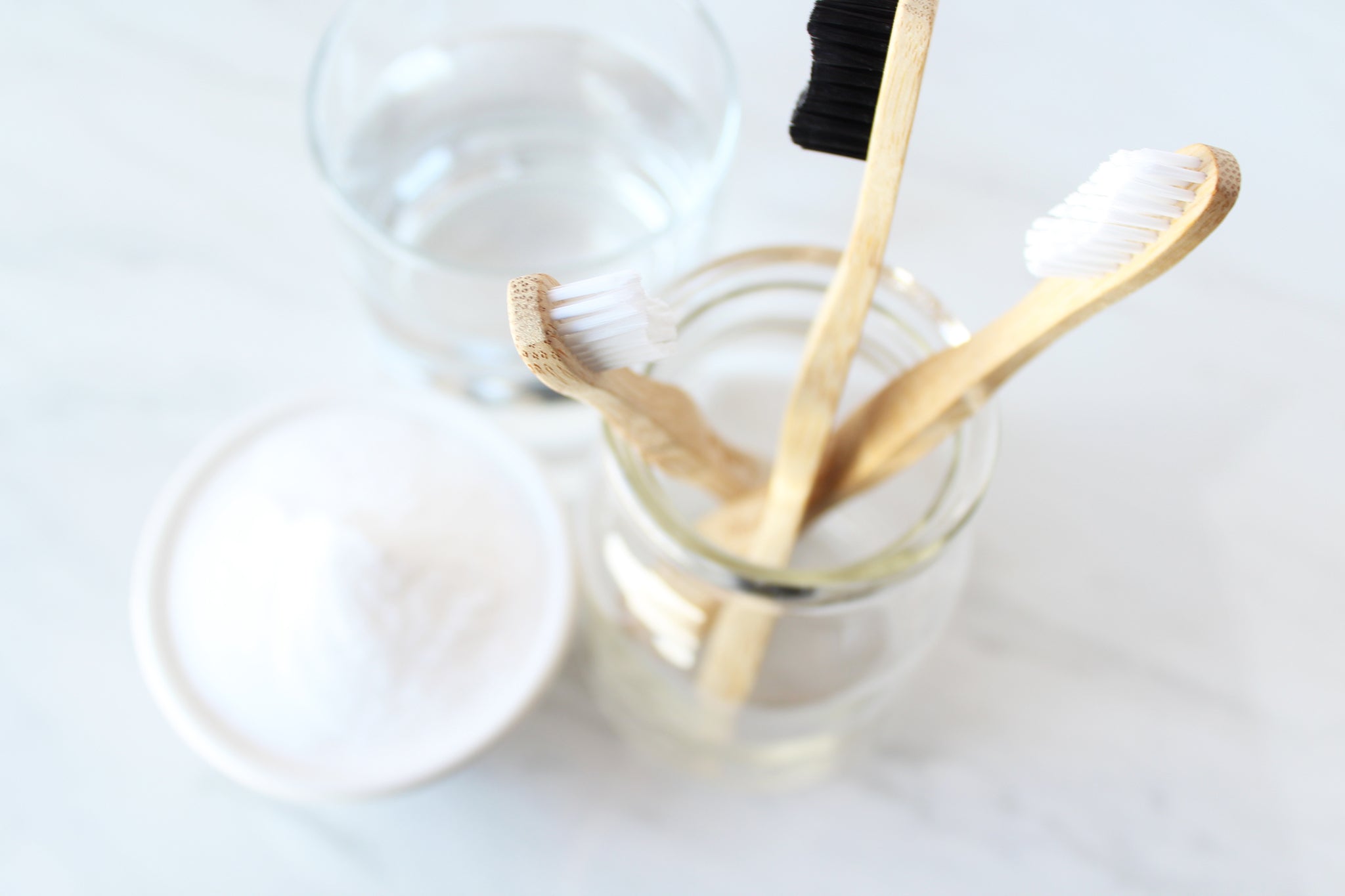 drei Bürste in einem Glas, neben ein Glas gefüllt mit Wasser und eine Schüssel mit einem weißen Pulver. Von oben aufgenommen.
