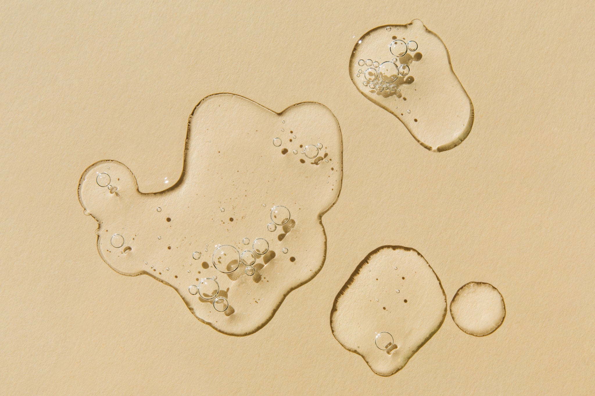 Transparente Tropfen Öl mit kleinen Luftblasen auf beiger Oberfläche