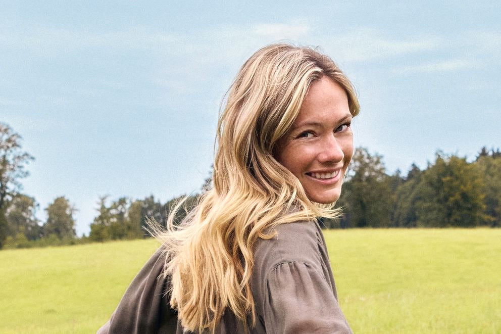 Blonde Frau lächelt über Schulter auf grüner Wiese, Outdoor-Porträt