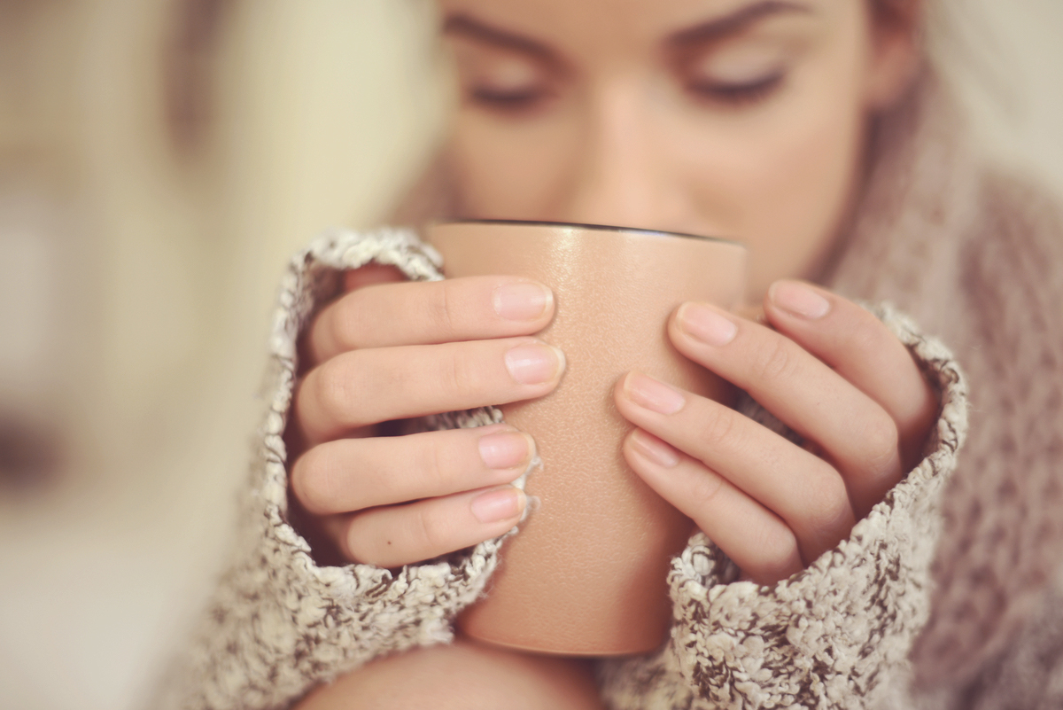 Erstmal ein heißer Tee Junge Frau mit warmen Cardigan hält eine Tasse in ihren Händen