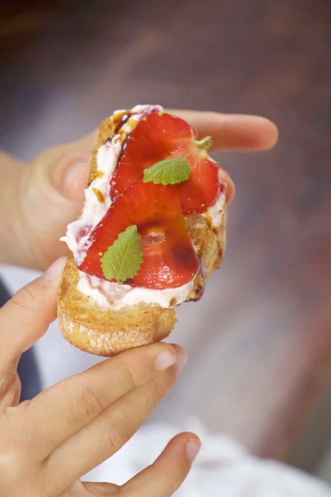 martina-obst-Erdbeeren-Erdbeere-Crostini-Snack-Snacks-Kind-Hand-magazin-rezepte kinderhaende halten baguettebrot mit frischkaese und frischen aufgeschnittenen erdbeeren